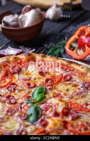 Aromatische Pizza mit Jagd Würstchen, Zwiebeln und Tomaten in der Nähe von mit Gemüse. Hintergrund bereit für Ihr Design. Pizza auf schwarzem Hintergrund Stockfoto