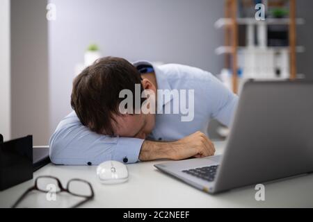 Junge Unternehmer mit Laptop am Schreibtisch schlafen im Büro Stockfoto