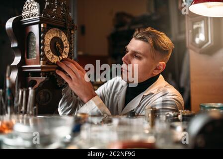 Uhrmacher stellt den Mechanismus der alte Wanduhr in der Werkstatt. Stockfoto