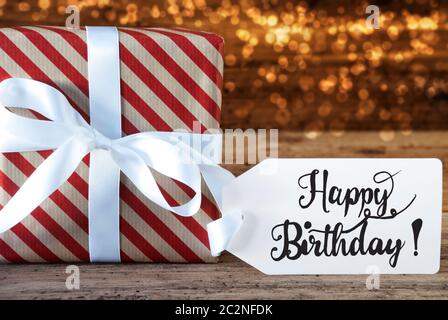 Ein Weihnachtsgeschenk mit Label mit englischen Kalligraphie Happy Birthday. Geschenkpapier mit Schleife und Lichter im Hintergrund Stockfoto