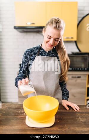 Junge Frau in Schürze fügt Zucker in einer Schüssel auf Holztisch. Süße Kuchen kochen Vorbereitung. Teig machen Stockfoto