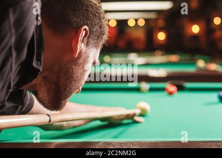 Mann versucht, den Ball im Billard zu schlagen. Billardzimmer im Hintergrund. Stockfoto