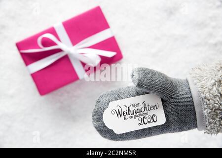 Etikett mit Deutschen Kalligraphie Frohe Weihnachten und ein Glueckliches 2020 bedeutet, frohe Weihnachten und einen guten Rutsch ins Jahr 2020. Grau Handschuh mit rosa Geschenk und Schnee B Stockfoto