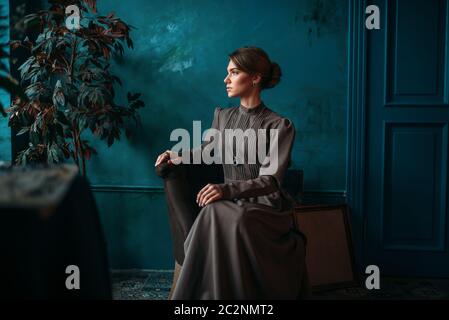 Schöne weibliche Poseur in Kleid sitzt auf einem Stuhl im Kunstatelier. Ölfarbe, Pinsel zeichnen Stockfoto