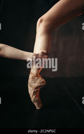 Ballerina Hand hält den Fuß in Pointe Schuhe, schwarz Holzboden. Ballerina im roten Kleid und schwarzen Praxis tanzen auf der Bühne im Theater Stockfoto