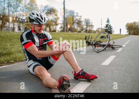 Männliche bycyclist fiel aus Fahrrad und schlug seine Knie, Radfahren am Radweg. Sportsman Fahrten auf dem Fahrrad Stockfoto