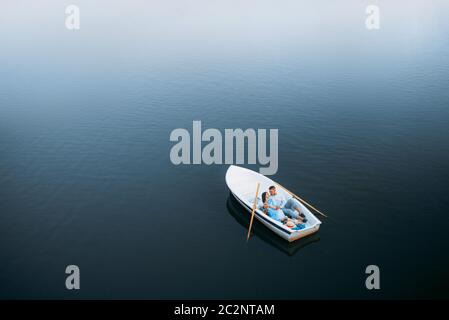 Liebespaar, das in einem Boot auf dem stillen See liegt, von oben gesehen. Romantische Treffen, Bootstour, Mann und Frau, die am Fluss entlang spazieren Stockfoto