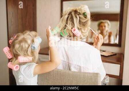 Kind macht eine lustige Frisur zu ihrer Mutter gegen einen Spiegel im Schlafzimmer zu Hause, Spielzeug, Friseursalon. Eltern fühlen, das Miteinander, die glücklichen Zeiten Stockfoto