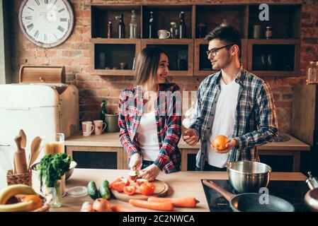 Junge Mann jongliert Orangen in der Küche, während Frau kochen Obst Frühstück. Mann und Frau Vorbereitung Gemüsesalat, glückliche Familie zusammen Stockfoto