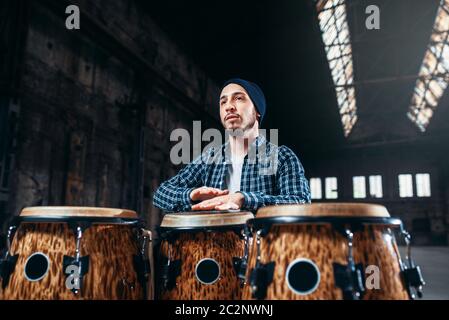 Männliche Schlagzeuger spielt auf hölzernen Trommel in big Factory Shop, Vorderansicht, Musiker in Bewegung. Bongo, musikalische Schlaginstrument, ethnische Musik Stockfoto