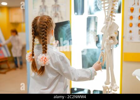 Kleines Mädchen in Uniform schaut auf die Röntgenaufnahme, spielt Arzt, Spielzimmer. Kind spielt Mediziner in imaginären Krankenhaus, Beruf lernen Stockfoto