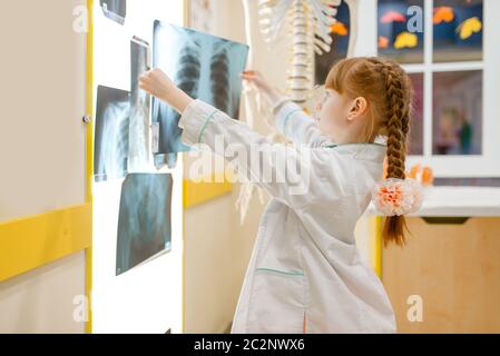 Kleines Mädchen in Uniform schaut auf die Röntgenaufnahme, spielt Arzt, Spielzimmer. Kind spielt Mediziner in imaginären Krankenhaus, Beruf lernen Stockfoto