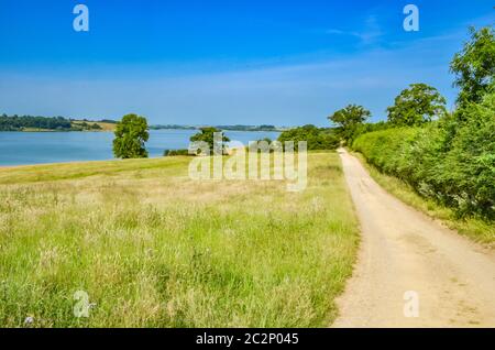 Ein Weg führt in Richtung Rutland Water, einem großen Stausee in Leicestershire. Mit blauem Himmel Gras und Bäumen. Stockfoto