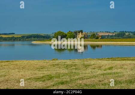 Niedrigwasser am Rutland Reservoir, das Küstenlinie und Bauruinen zeigt. Blauer Himmel und Schafe am Wasser. Stockfoto