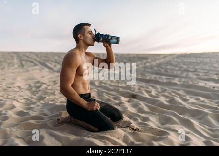 Männliche Sportler trinkt Wasser nach dem Training in der Wüste an sonnigen Tag. Starke Motivation im Sport, Kraft Outdoor-Training Stockfoto