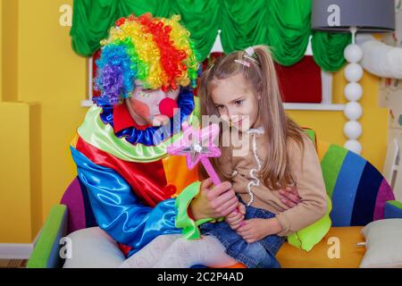 Kleines Mädchen spielt mit fröhlichen Clown in lustigen Kostüm. Freundschaftskonzept Stockfoto