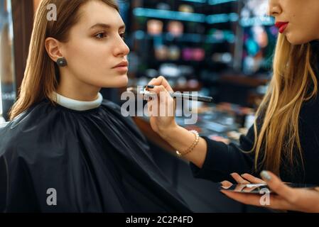 Visagiste gilt Puder mit Pinsel, Frau in Make-up-Shop. Weibliche Client im Beauty Salon Stockfoto