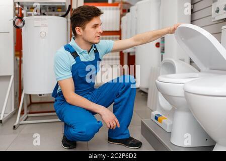 Klempner in Uniform die Wahl der Toilette bei der Vitrine in Klempnerladen. Mann mit Notebook Kauf Sanitärtechnik im Geschäft Stockfoto