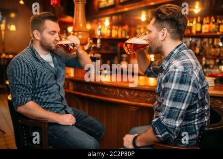 Zwei lächelnde männliche Freunde trinkt Bier an der Theke im Pub. Bärtige Männer mit Tassen Spaß in bar, gute Freundschaft Stockfoto