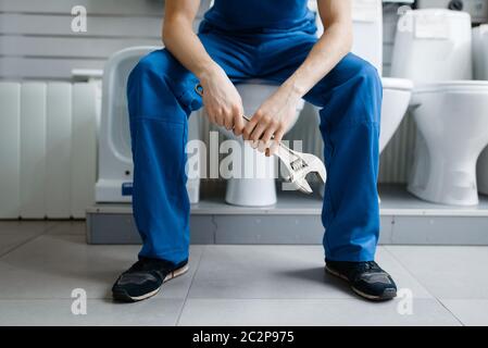 Klempner in Uniform sitzt auf der Toilette bei der Vitrine in Klempnerladen. Mann kauft Sanitär-Engineering-Werkzeuge und Geräte im Geschäft Stockfoto