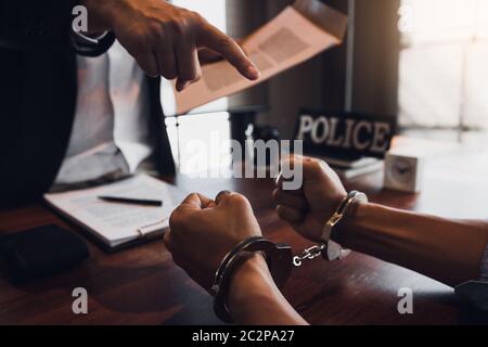 Der Polizist zeigte die Handschellen und hielt die Dokumente, um den Angeklagten in einem Betrugsfall zu verhaften. Stockfoto