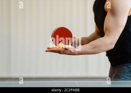 Mann mit Ping pong Schläger vorbereiten, einen Ball zu schlagen, Training im Innenbereich. Männliche Person in Sportbekleidung, Training im Tischtennis club Stockfoto