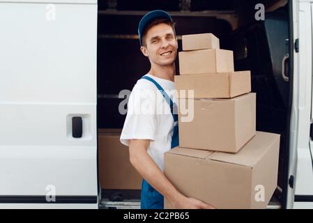 Postbote in Uniform entlädt das Auto mit Paketen, Lieferservice. Mann steht an Pappverpackungen im Fahrzeug, männlich liefern, Kurier oder Versand jo Stockfoto
