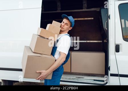 Postbote in Uniform entlädt das Auto mit Paketen, Lieferservice. Mann steht an Pappverpackungen im Fahrzeug, männlich liefern, Kurier oder Versand jo Stockfoto