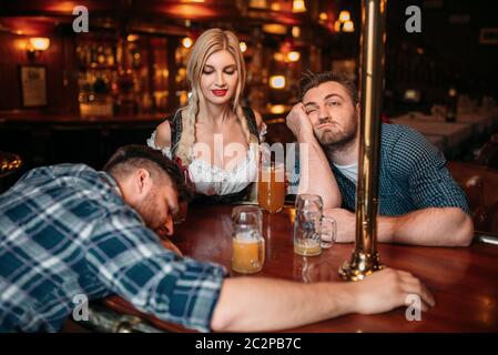 Zwei Betrunkene Freunde an der Theke mit Bierkrügen in Pub schlafen, hübsche Kellnerin auf Hintergrund, oktoberfest Urlaub. Männliche Personen trinken in der Bar, Ba Stockfoto