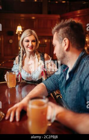 Betrunkener Mann mit Bierkrug und hübsche Kellnerin an der Zähler im Pub, oktoberfest Urlaub. Männliche Person trinken in der Bar, bardame in traditionellen Retro sty Stockfoto