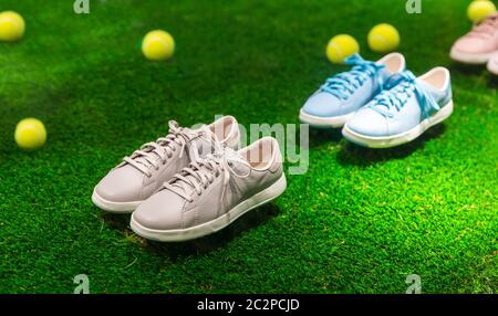 Wenige Paar farbige Sportschuhe und gelbe Tennisbälle auf grünem Gras mit Sonnenstrahlen. Stockfoto