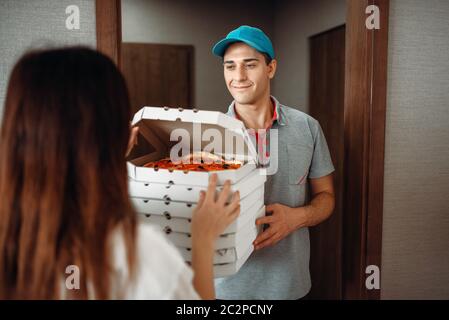 Lieferung Mensch zeigt Frische und heiße Pizza für die weiblichen Kunden vor der Tür, Bereitstellung von Service. Von Pizzeria und die Frau in der Nähe der Einfahrt zum Ap liefern Stockfoto