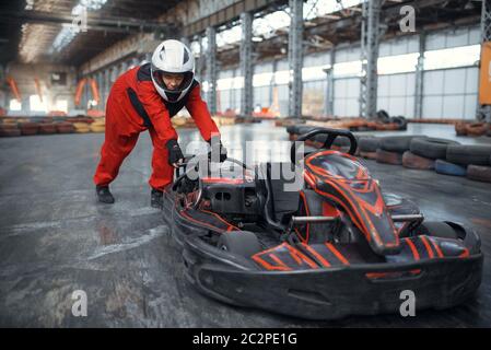 Racer in Helm schieben ein Go Kart Auto, Karting Auto Sport Indoor. Speed Race auf engem Go-Kart Track mit Reifenbarriere. Schnelle Fahrzeug-Wettbewerb, hoch Stockfoto