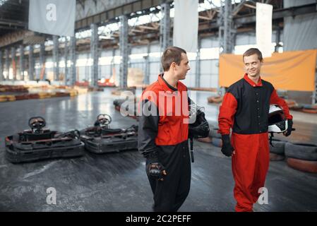 Zwei Kart-Rennfahrer hält Hemets, Karting Auto Sport Indoor. Speed Race auf engem Go-Kart Track mit Reifenbarriere. Schnelle Fahrzeugkonkurrenz Stockfoto