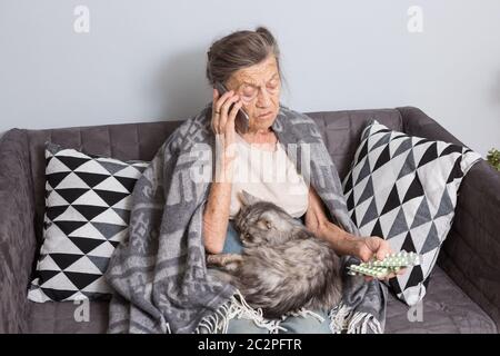Kranke ältere Frau, die zu Hause Medizin nimmt. Ältere Frau im Gespräch auf Handy, während sie auf Medizin im Schlafzimmer. Rentner Stockfoto