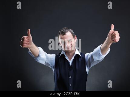 Glücklich Kaufmann zeigt beide Daumen sich über grau Stockfoto