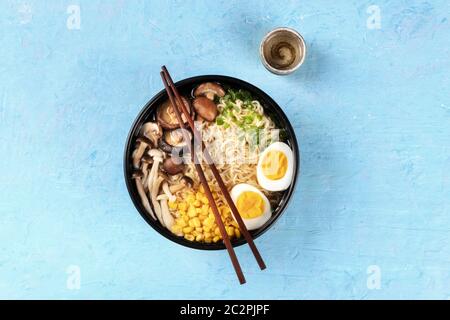 Ramen. Soba Nudeln mit gekochten Eiern, Shiitake-Pilzen und Gemüse, von oben auf blauem Hintergrund mit Essstäbchen geschossen, Stockfoto