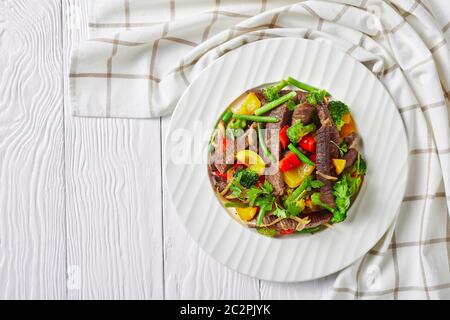 Rindfleisch Fajitas auf einem weißen Teller mit Brokkoli, grünen Bohnen, gelben und roten Paprika, Petersilie, Zwiebel auf weißem Holzhintergrund mit einer Küchenschale Stockfoto