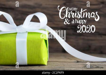 Etikett mit englischen Kalligraphie frohe Weihnachten und einen guten Rutsch ins Jahr 2020. Eine grüne Geschenk mit weißen Bogen. Braun Holz- Hintergrund Stockfoto
