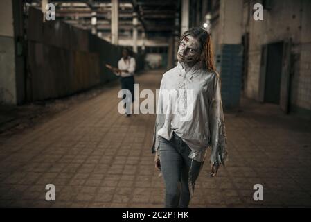 Mann mit Axt aufholen weiblichen Zombie in verlassenen Fabrik, beängstigend Ort. Horror in der Stadt, gruselige Krabbeltiere, Weltuntergangsapokalypse, blutige böse Monster Stockfoto