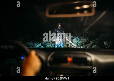 Serienmaniac in Hockey Maske mit blutigen Baseballschläger in Kette in der Weise der weiblichen Opfer auf dem Auto in der Nacht eingewickelt. Horror, Mörder Stockfoto