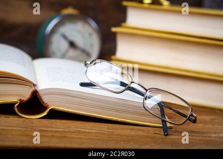 Öffnen Sie Tutorial mit Brille auf dem Tisch im Publikum. Bildungskonzept - Bücher auf dem Schreibtisch im Auditorium. Auf einem hölzernen Hintergrund. Selektiv fo Stockfoto