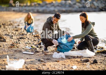 Team von engagierten und lächelnden Freiwilligen sammeln Müll am Strand Stockfoto