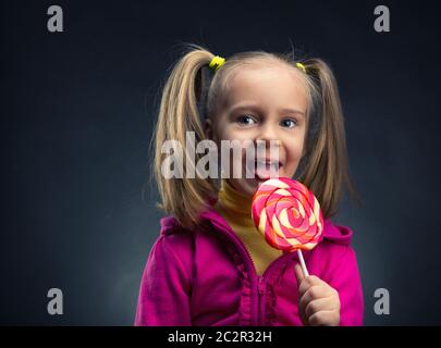 Glückliche kleine Mädchen essen Lutscher über dunkel Stockfoto