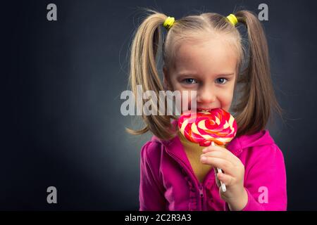 Glückliche kleine Mädchen essen Lutscher auf dunklem Hintergrund Stockfoto