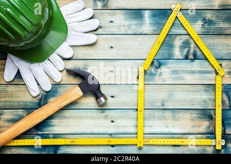 Blick von oben der Tischler hammer, Helm und Leder Arbeitshandschuhe auf einem antiken Holztisch. Haus Konzept mit dem Messgerät. Industrie Bau Stockfoto