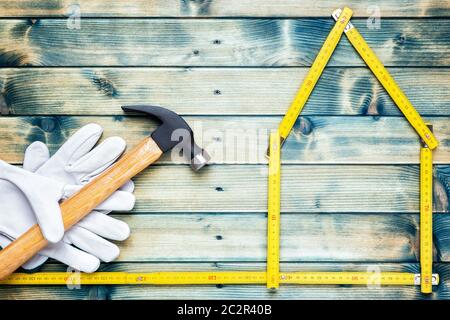 Blick von oben der Tischler Hammer und Leder Arbeitshandschuhe auf einem antiken Holztisch. Haus Konzept mit dem Messgerät. Industrie Bau- und Stockfoto