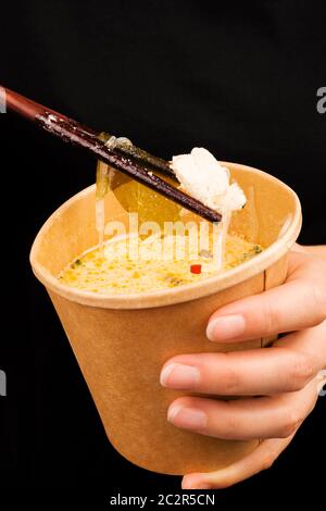 Frau, die tom-yam-Suppe in einer Tasse zum Mitnehmen isst. Traditionelle asiatische Küche. Stockfoto