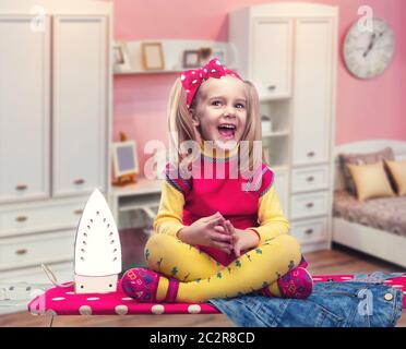 Glückliches kleines Mädchen sitzt auf dem Bügelbrett lächelnden Stockfoto