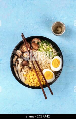 Ramen. Soba Nudeln mit gekochten Eiern, Shiitake-Pilze und Gemüse, über Kopf Schuss auf einem blauen Hintergrund mit Essstäbchen, a Stockfoto
